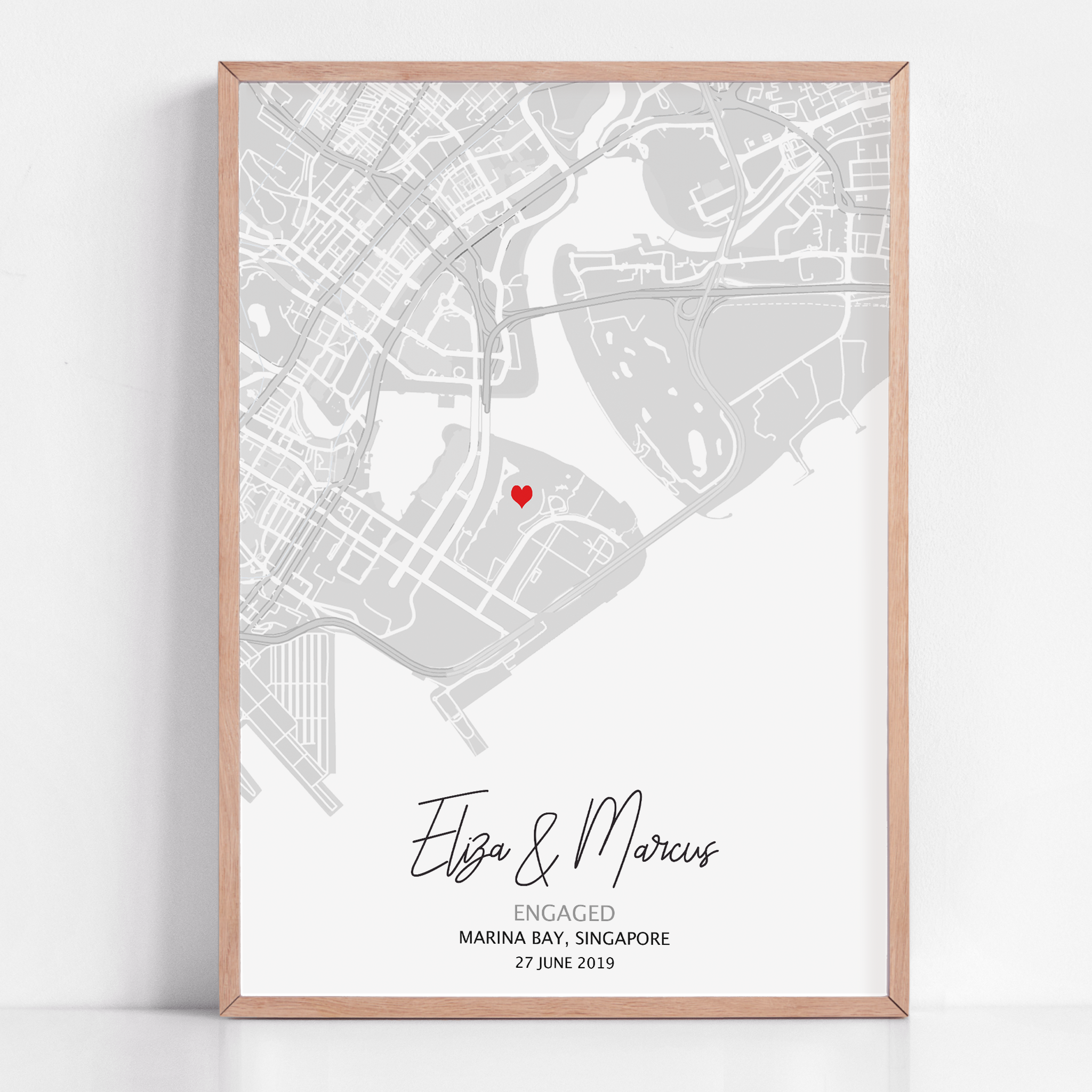 Custom engagement map print showing a map of the proposal location with a small red heart marker, personalized cursive names and date text below on white background
