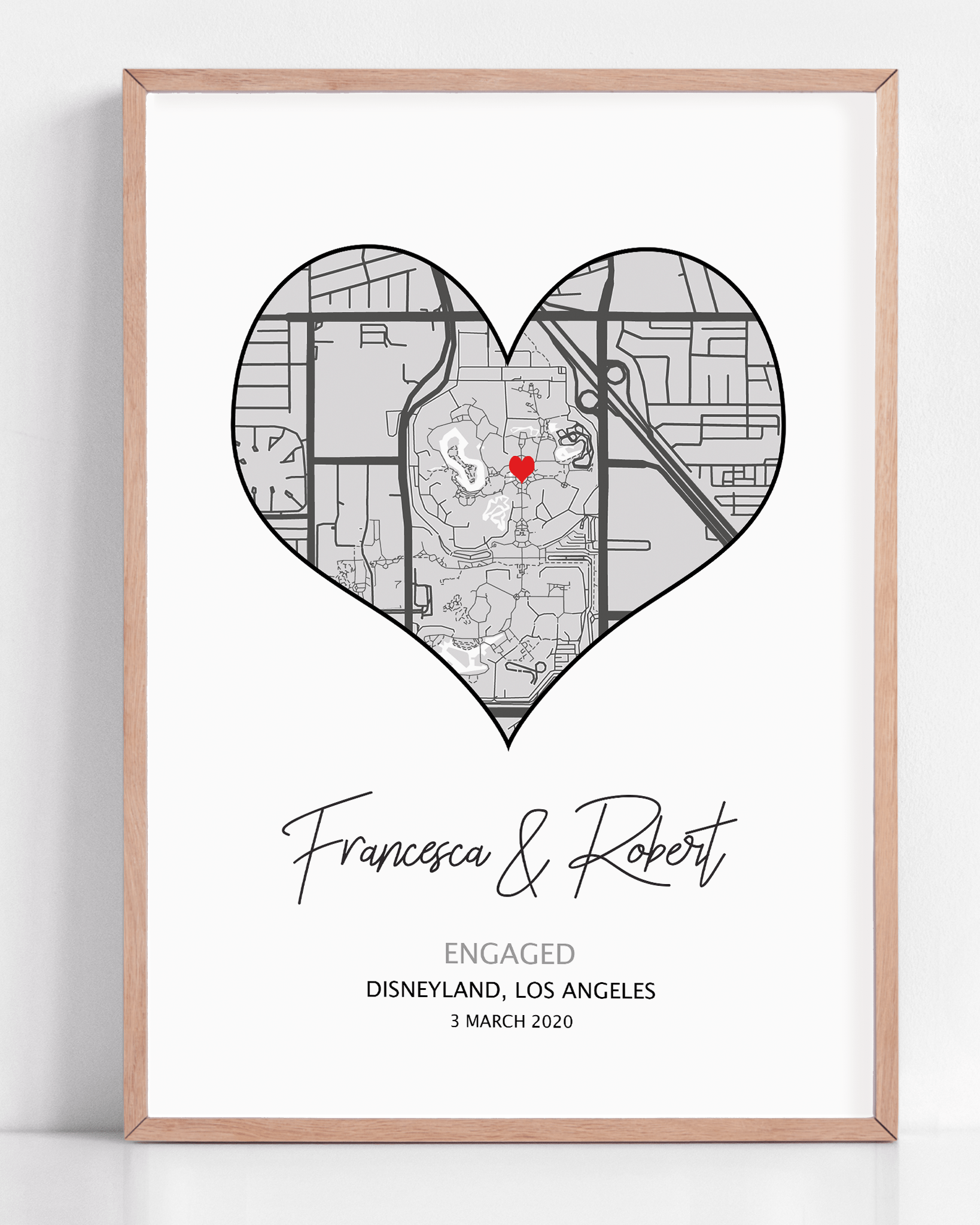 Heart-shaped engagement map print with a red heart marking the proposal location, customized with couple’s names and date in elegant script below the map on a white background.