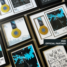 A collage of framed custom 2026 Sydney Marathon memorabilia, including medal display frames, event maps, and illustrated prints, arranged on a beige wall. A dark overlay in the lower right reads '2026 OFFICIAL PARTNER'.