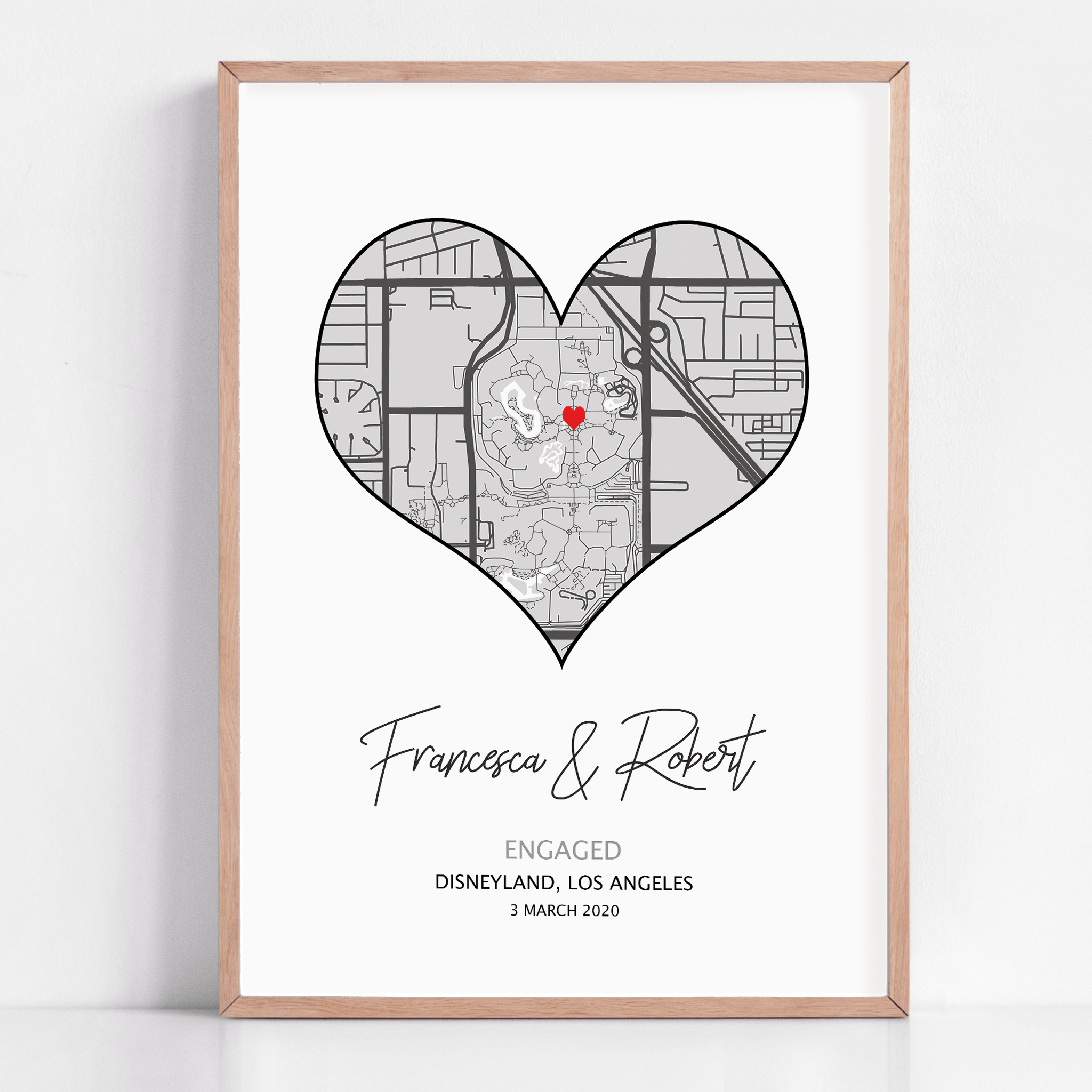 Heart-shaped engagement map print with a red heart marking the proposal location, customized with couple’s names and date in elegant script below the map on a white background.